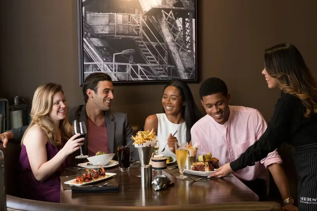 Waitress serves food to four happy diners in a lively restaurant.