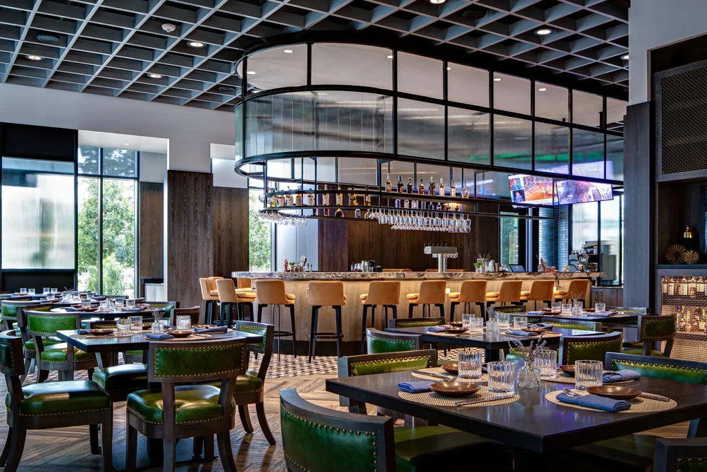 Modern restaurant dining area and bar with green chairs.