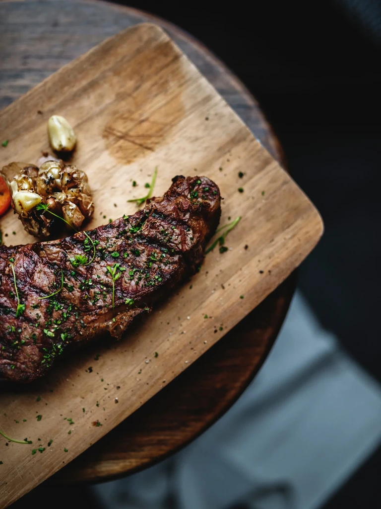 Perfectly cooked steak with herbs, pepper, and roasted garlic on a wooden board.