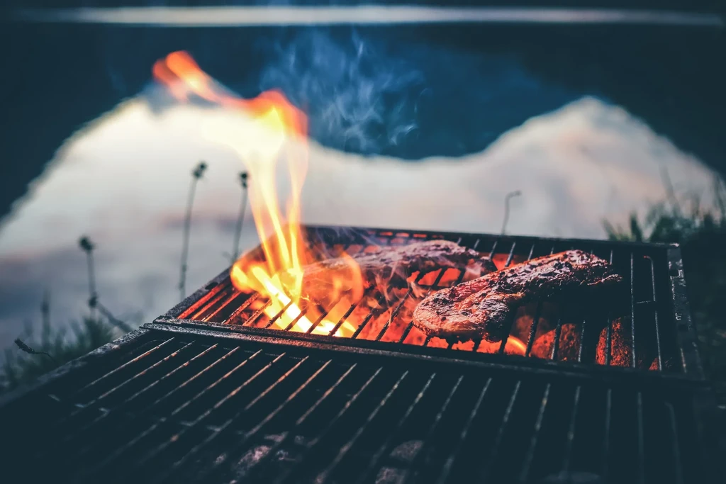 Meat sizzling on a barbecue grill over glowing coals and flames.