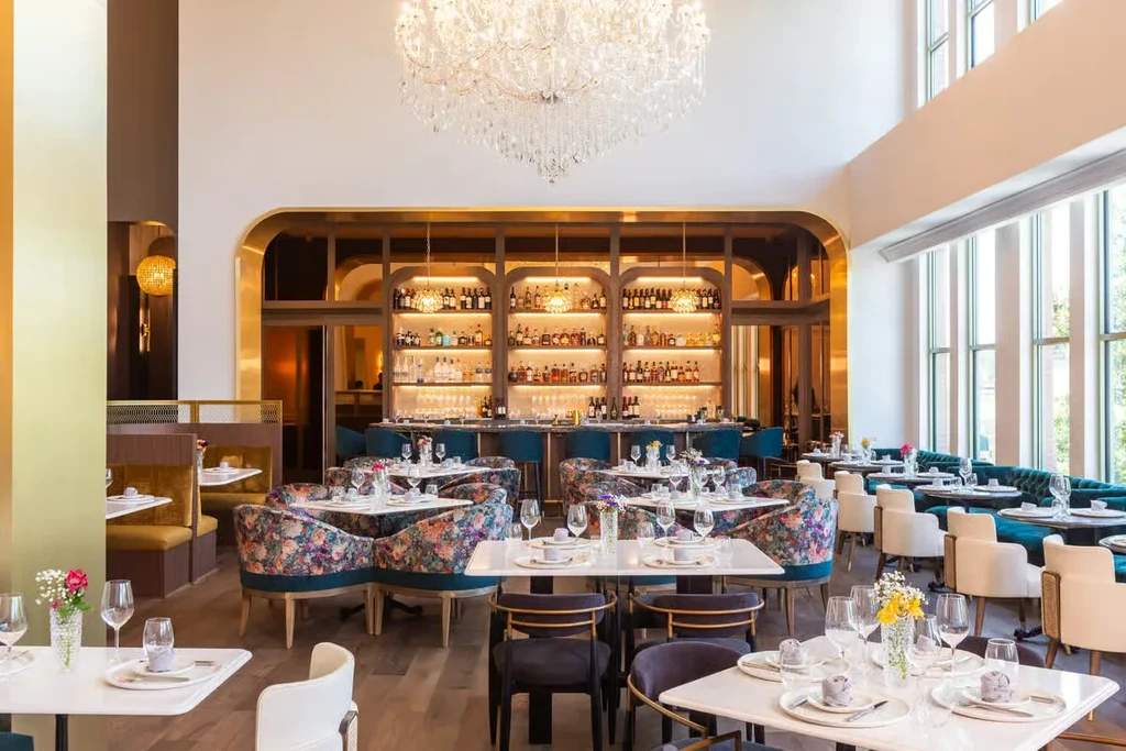 Elegant, empty restaurant with set tables, crystal chandelier, and well-stocked bar.
