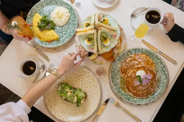 Overhead view: Brunch table laden with diverse foods, drinks, and hands.