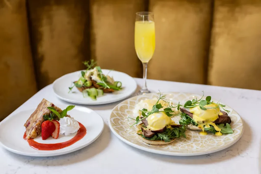 Brunch spread with berry cake, Eggs Benedict, avocado toast, mimosa.