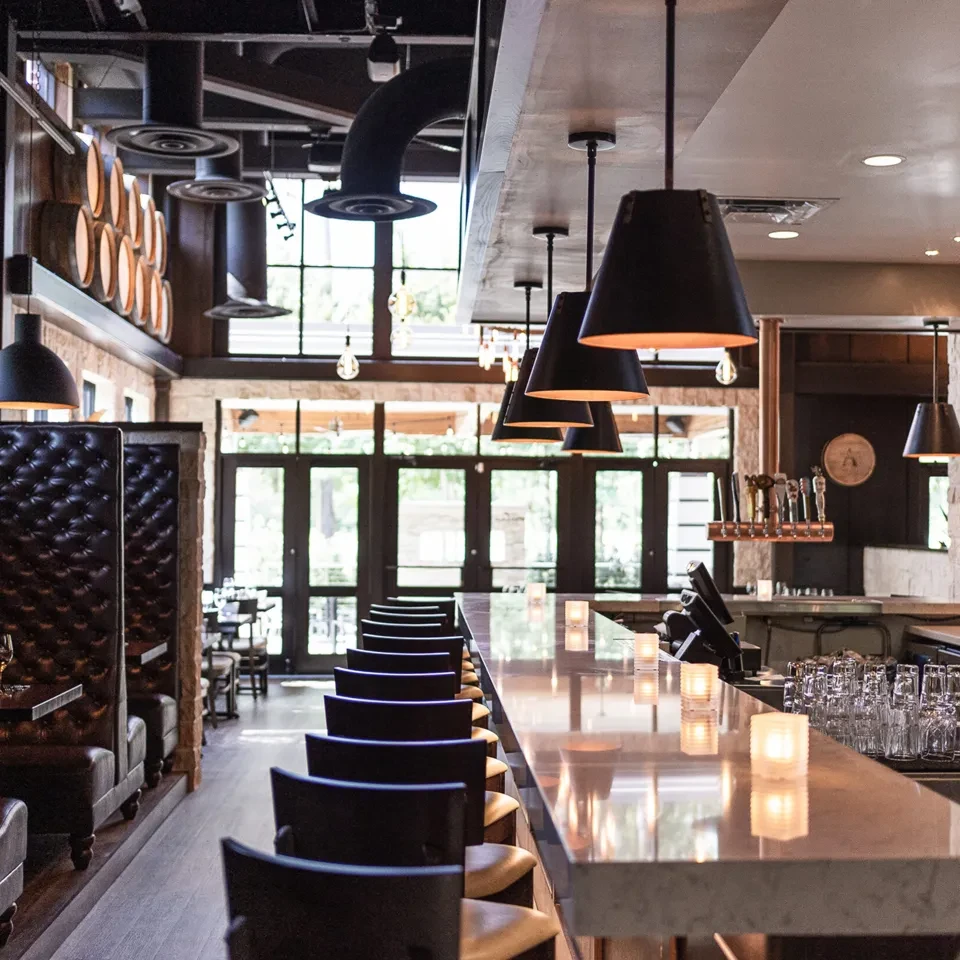 Warm, industrial-chic bar interior with polished counter and tufted leather booths.