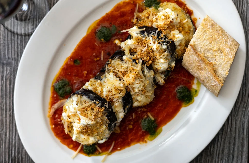 Plated eggplant rolls with cheese, tomato sauce, pesto, and bread.