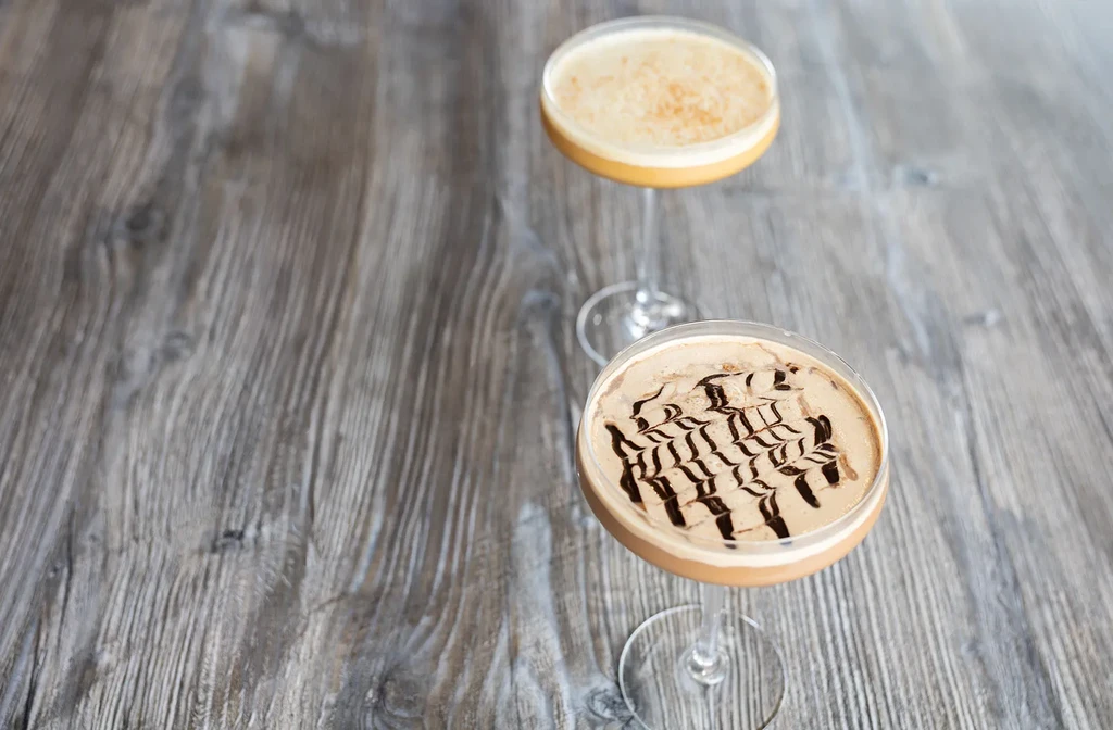 Two artfully presented creamy drinks in martini glasses on rustic wood.