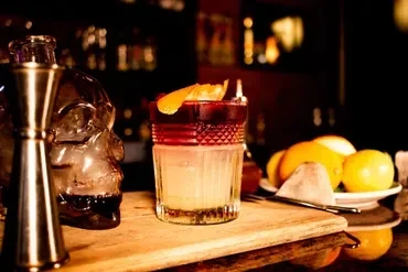 Cocktail in textured glass with orange peel on a wooden bar.