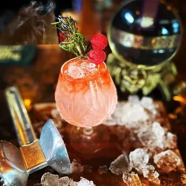 Pink cocktail in a textured glass garnished with rosemary and raspberries.