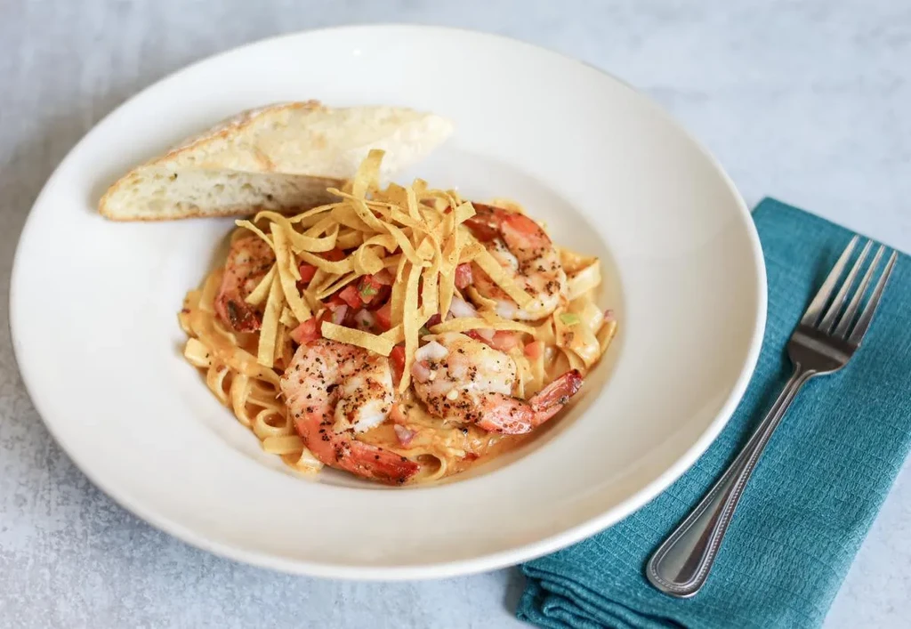 Creamy pasta with seasoned shrimp, tomatoes, crispy strips, and bread.
