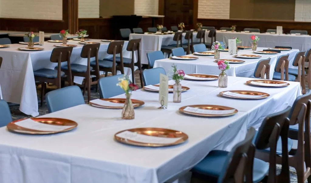 Dining room with long tables, copper chargers, and colorful flower centerpieces.