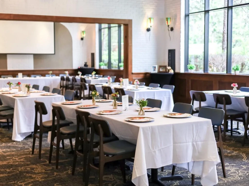 Well-lit dining hall with white tables, floral arrangements, and windows.