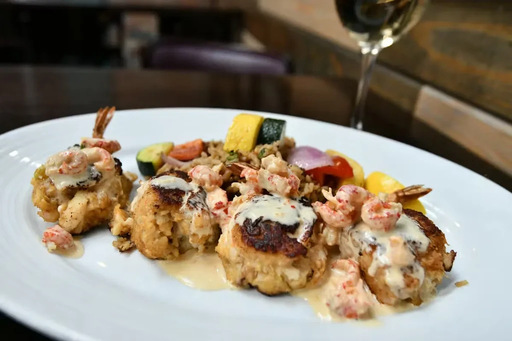 Pan-seared crab cakes with crawfish, creamy sauce, and colorful vegetable rice.