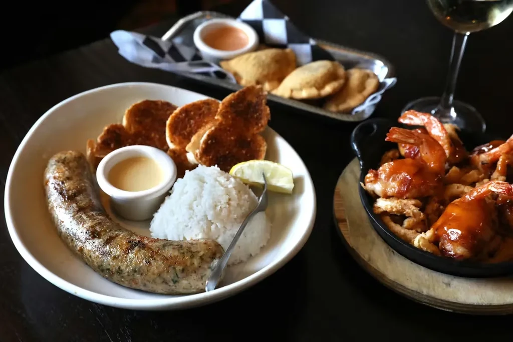 Grilled sausage, shrimp, empanadas, and white wine on a restaurant table.