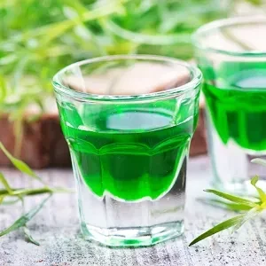 Close-up of a shot glass with layered vibrant green liquid.