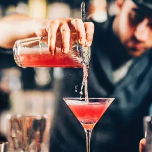 Bartender pours a pink drink from a shaker into a martini glass.