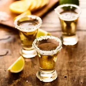 Three tequila shots, two with salt rims, and a lime wedge.