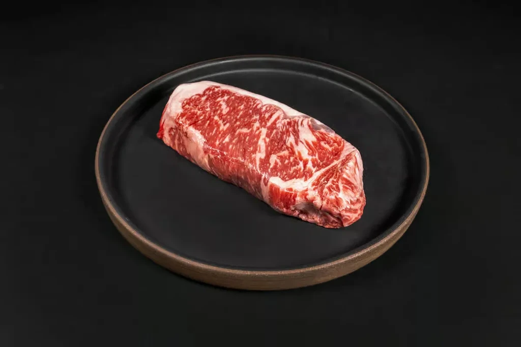 Extensively marbled raw steak on a dark ceramic plate.