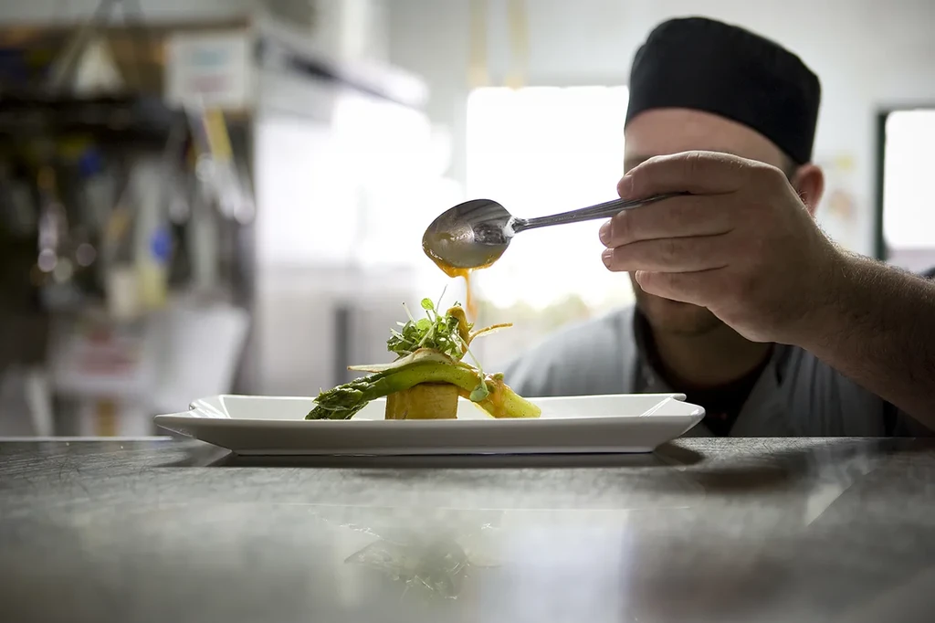 Close-up of chef garnishing asparagus and microgreens with orange sauce.