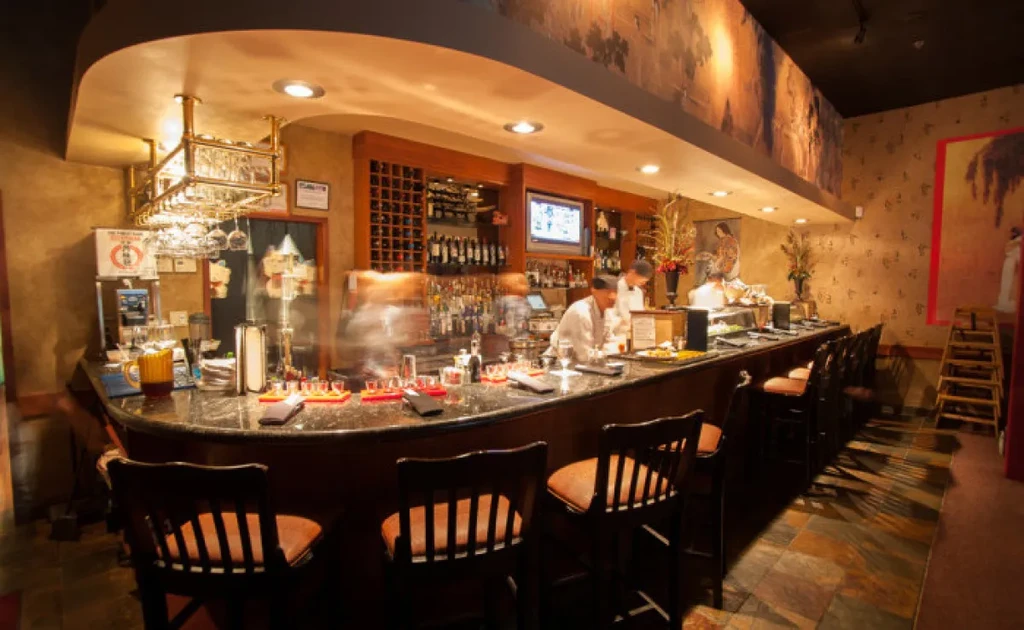 Restaurant bar with dark granite counter, stocked liquor, and blurred staff.