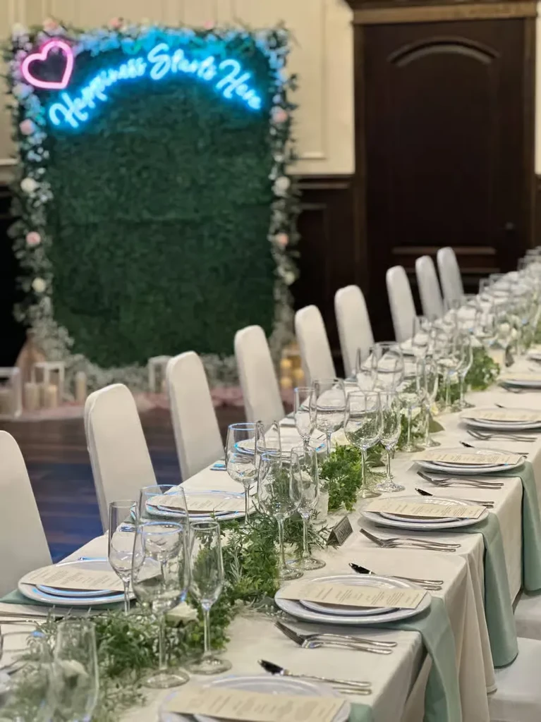 Set dining table with green garland, sage runners, and a floral 'Happiness' sign.