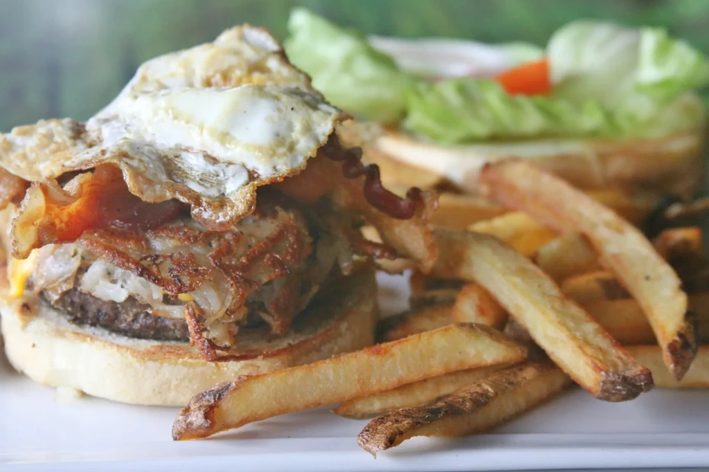 Gourmet burger with fried egg, bacon, and fries on a white plate.