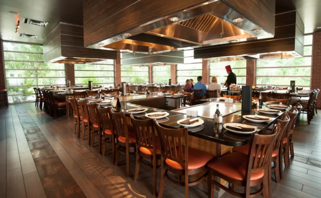 Modern Teppanyaki restaurant interior, chef cooks at grill for guests.