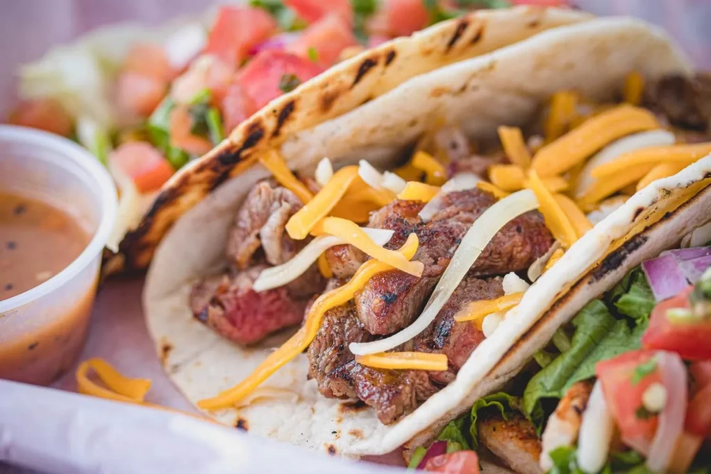 Close-up of three steak tacos with cheese, onion, and sauce.