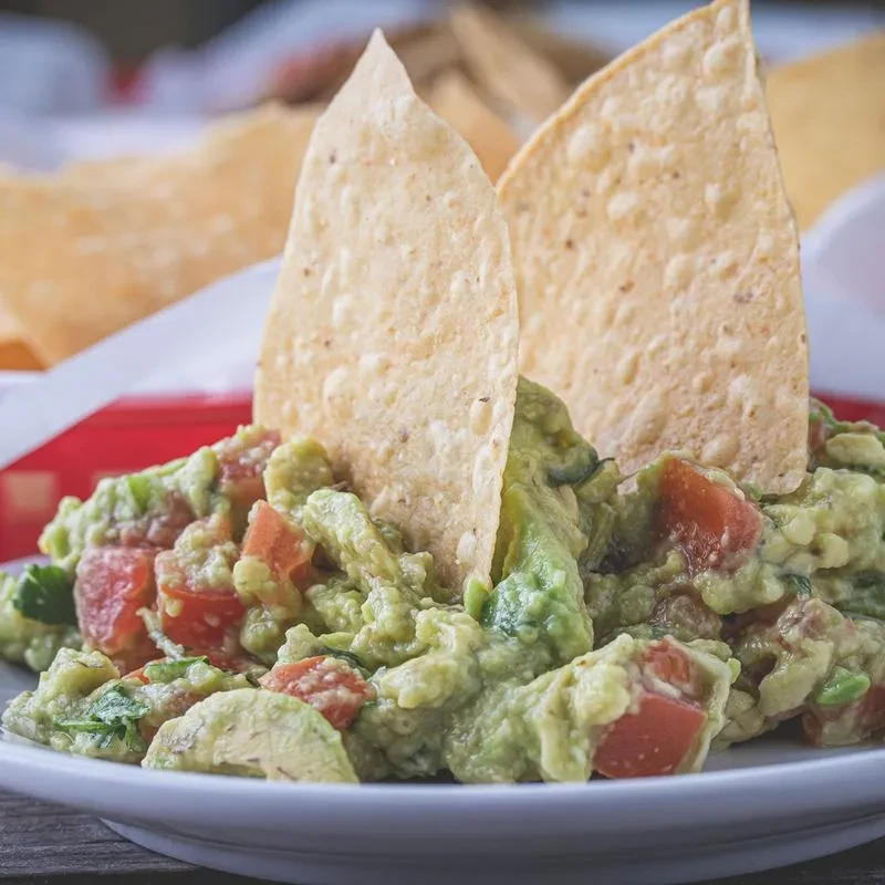 Guacamole with two large tortilla chips standing upright in it.