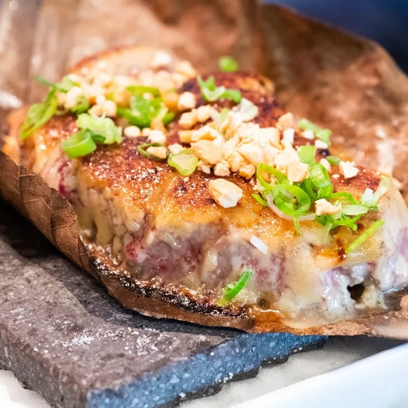 Seared meat on a leaf, garnished with green onions and peanuts.