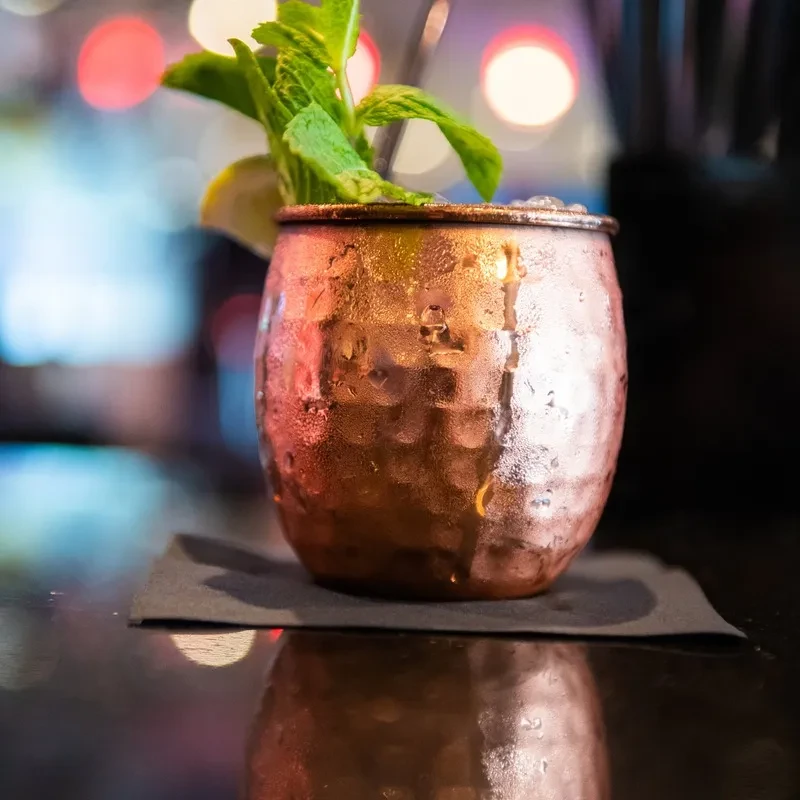 Frosted copper mug with mint and lemon on a bar counter.