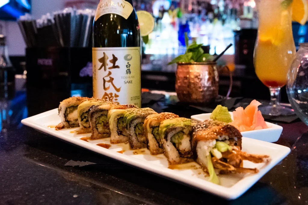 Sushi platter with wasabi, pickled ginger, and blurred drinks.
