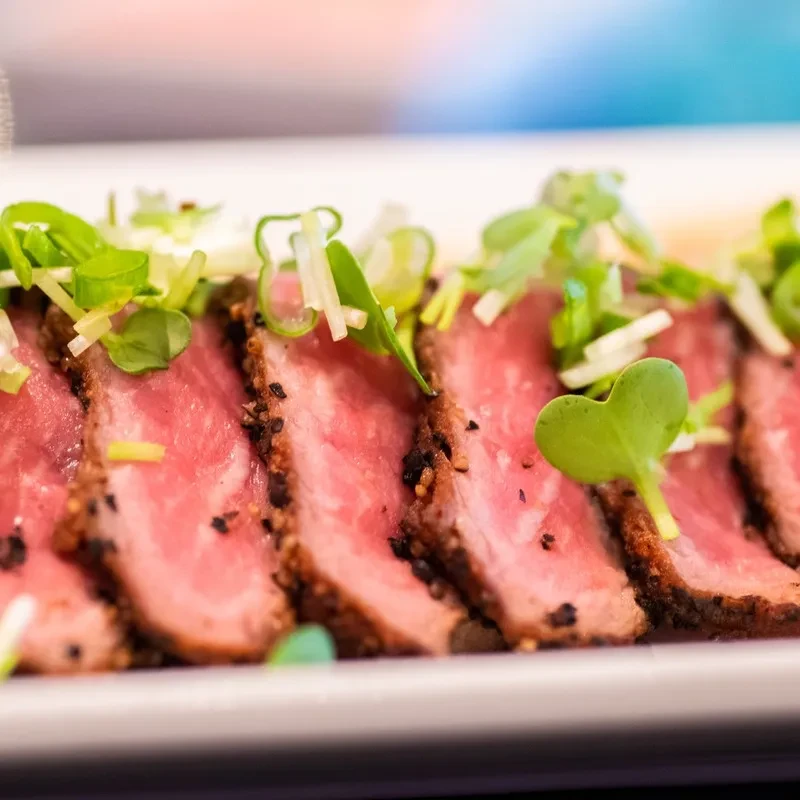 Slices of seared meat with a pink interior and green garnish.