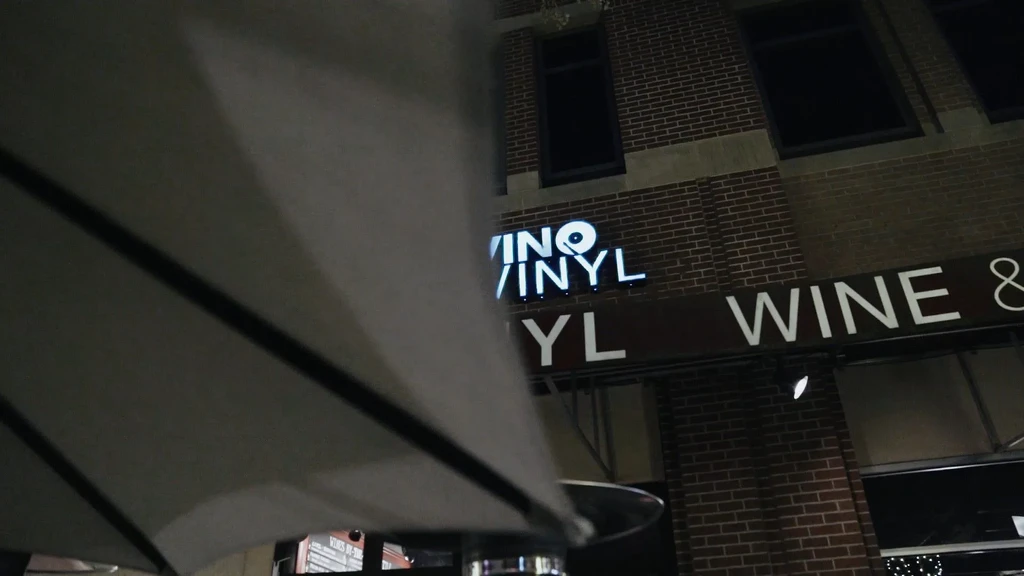 Exterior of building at night with illuminated "VINO VINYL WINE &" sign.