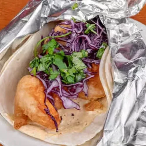 Fish taco with battered fish, purple cabbage, and cilantro.
