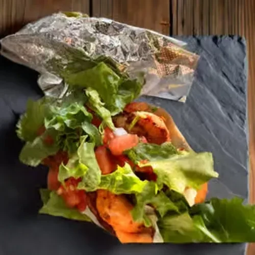 Taco or wrap with lettuce, tomatoes, and meat on a dark plate.