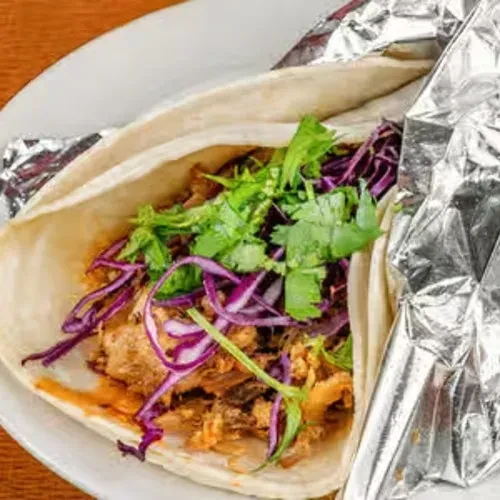 Taco or burrito with meat, cilantro, and cabbage on a white plate.