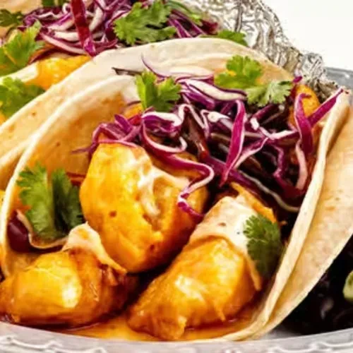 Close-up of tacos with fish, cabbage, sauce, and cilantro.