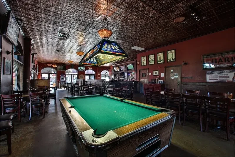 Empty pub interior with a green pool table and ornate tin ceiling.