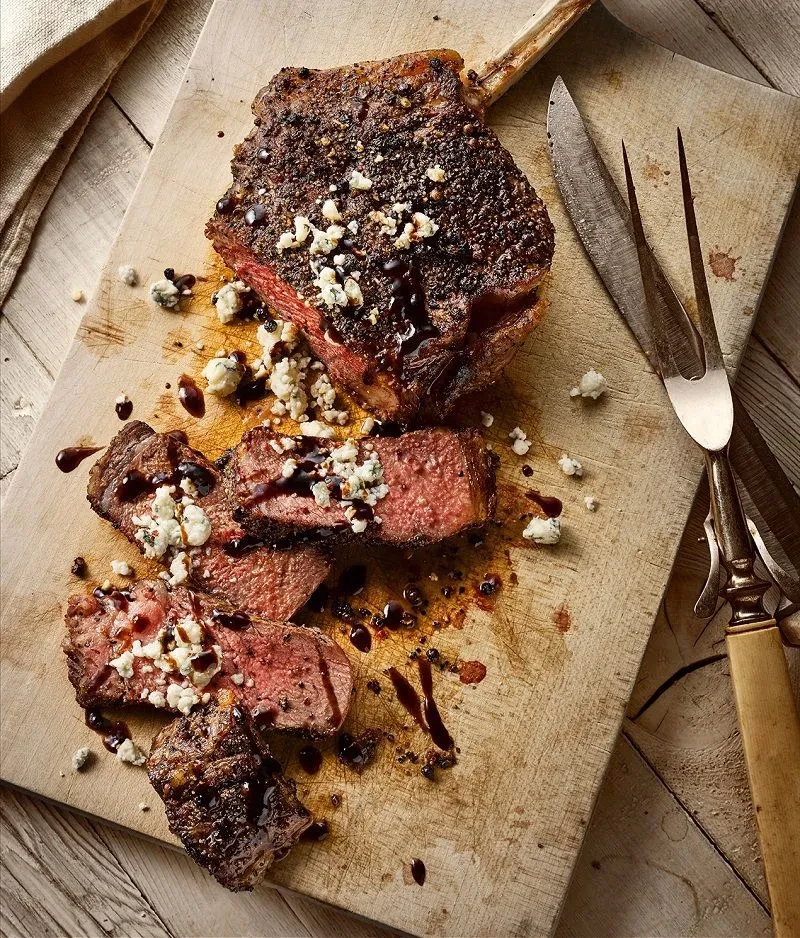 Tomahawk steak, sliced medium-rare, with blue cheese and dark sauce.