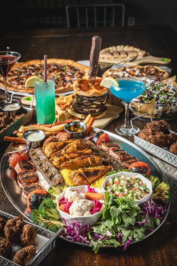 Lavish spread of grilled meats, falafel, burgers, pizzas, and cocktails.