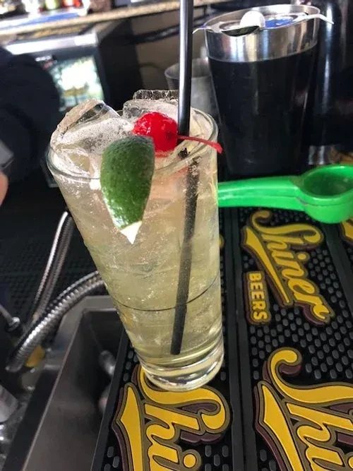 Iced golden cocktail with cherry and lime on a bar mat.
