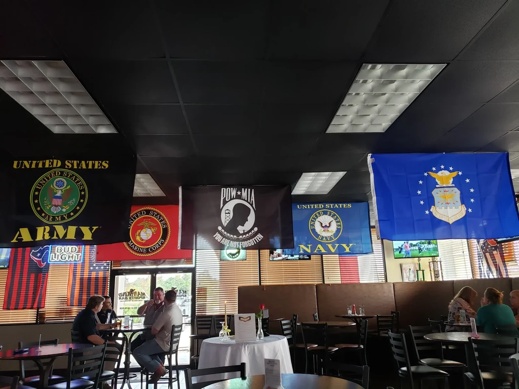 U.S. military flags hang from a dark ceiling in a restaurant.