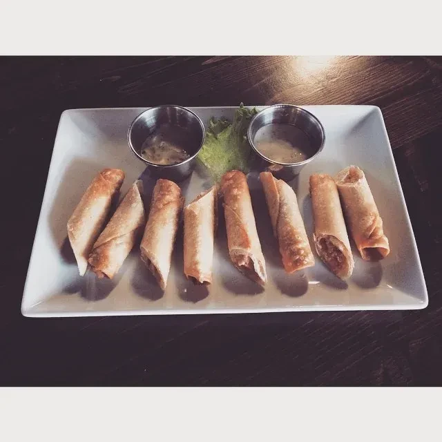 Eight spring rolls, two dipping sauces, and lettuce on a white plate.