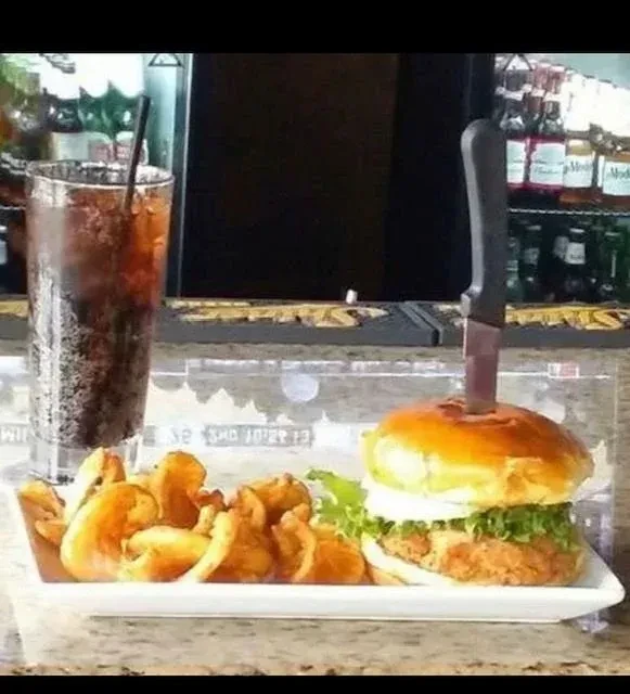 Burger with curly fries and a drink in a bar setting.