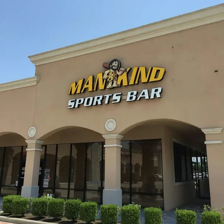 Exterior of a "MAN KIND SPORTS BAR" building under a blue sky.