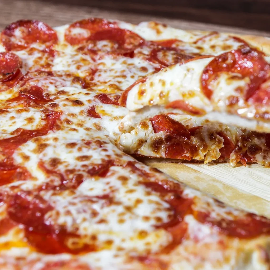 Close-up of a pepperoni pizza with a slice being lifted.
