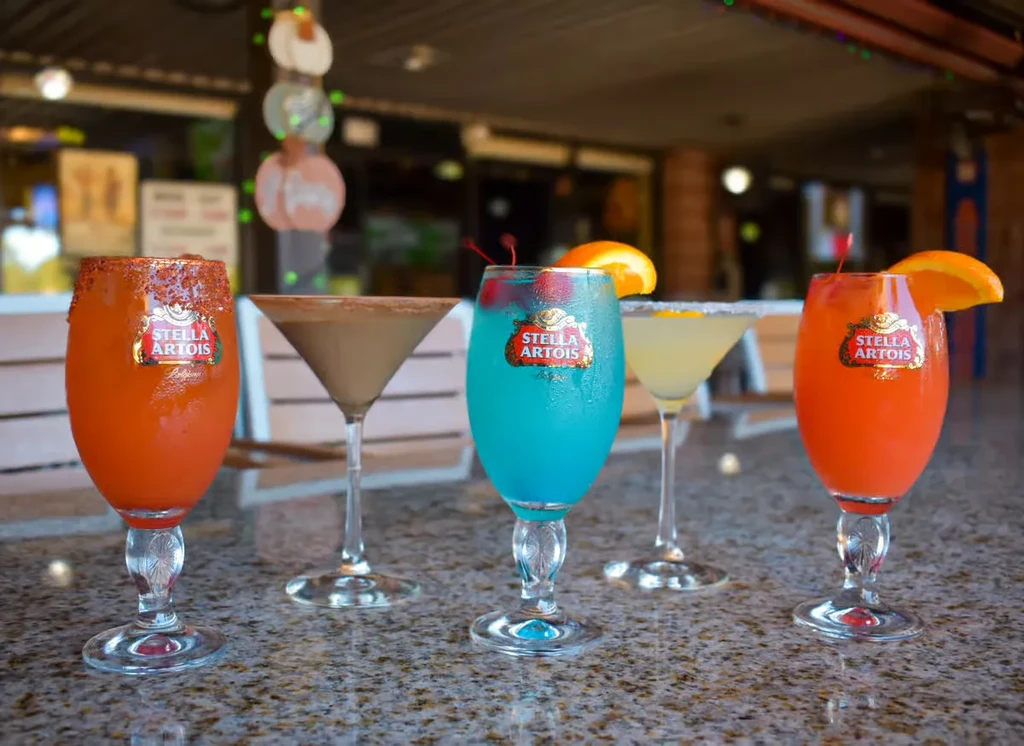 Five vibrant cocktails in Stella Artois and martini glasses on a counter.