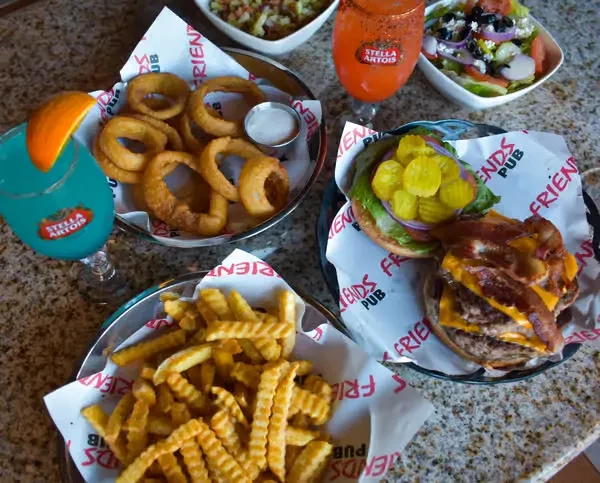 Overhead shot: double burger, fries, onion rings, drinks, and Greek salad.