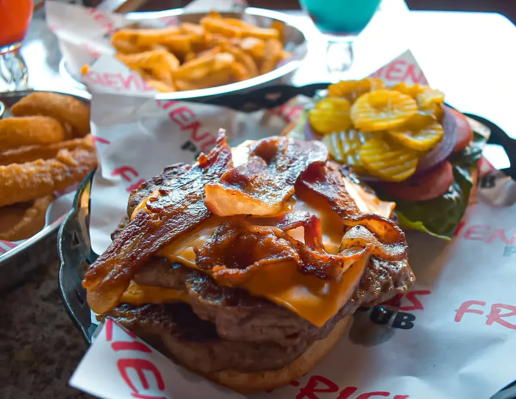 Bacon cheeseburger with separate bun, fries, and onion rings in baskets.