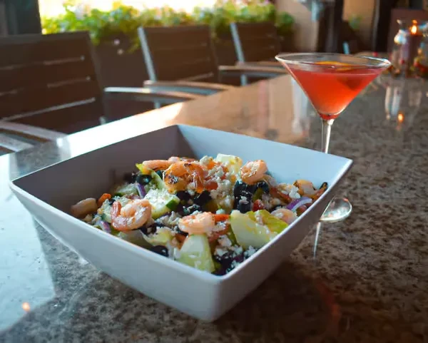 Grilled shrimp salad and pink cocktail on a speckled granite counter.